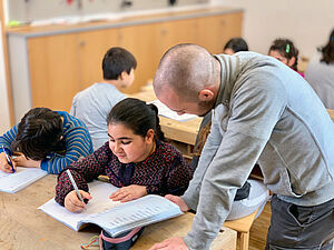 Schulkinder mit Lehrer der ins Heft schaut